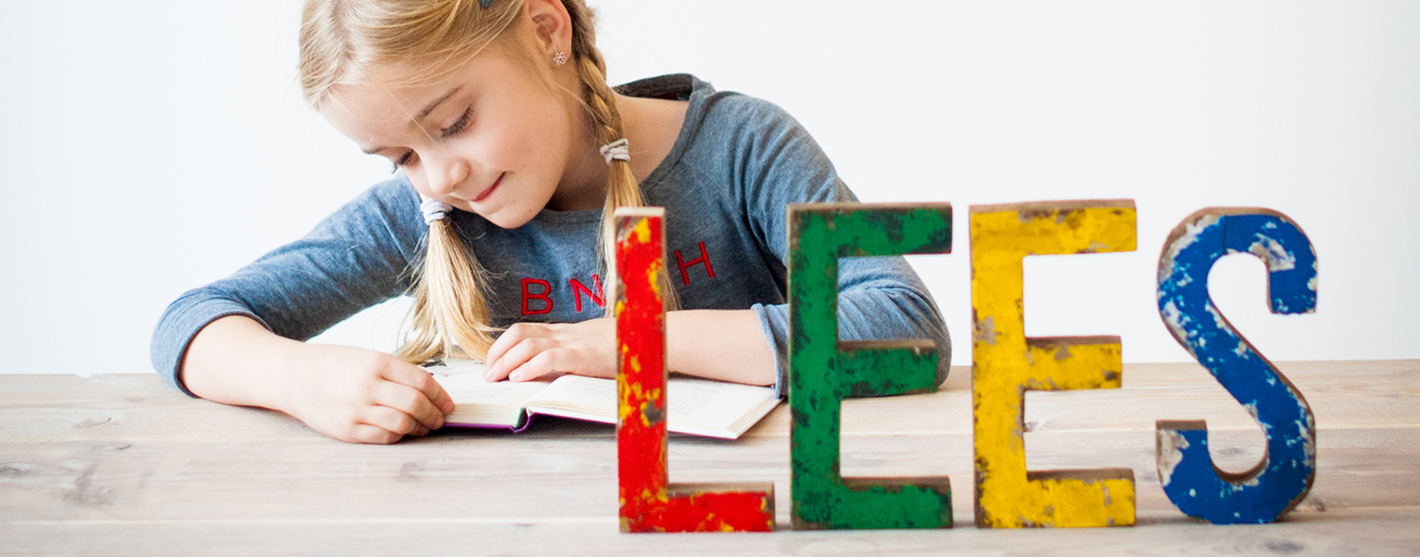 Kind aan het schrijven, met grote gekleurde letters LEES op tafel